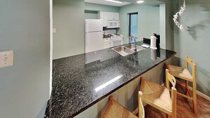 A kitchen with a black granite countertop, white cabinets, a microwave, and a stove. There are two wooden chairs with woven seats. - Watercolor Skies | Cozy, Waterfront (Corpus Christi)