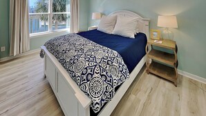 A bedroom with a bed, two bedside tables, a window with curtains, and a view of palm trees outside. - Papa's Paradise | Partial Beach Views (Galveston)