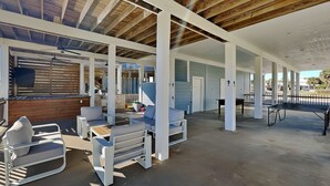 A covered outdoor area with white furniture, a ping pong table, and a view of a building with blue siding. - Papa's Paradise | Partial Beach Views (Galveston)