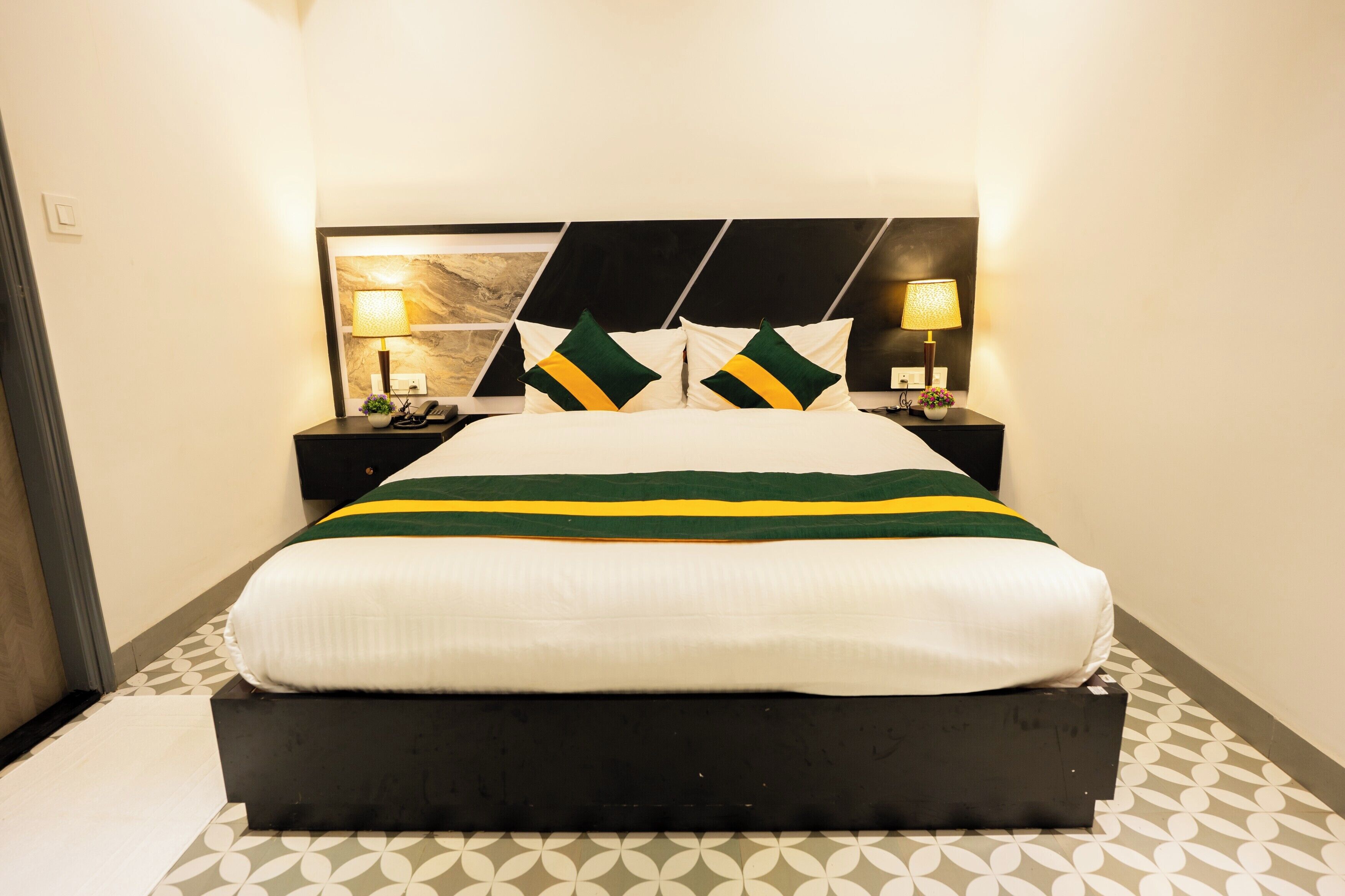 Une chambre d’hôtel avec un lit, deux tables de chevet et une tête de lit ornée d’un motif géométrique.