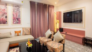 Una sala de estar moderna con un sofá, dos sillones estampados, una mesa de centro con fruta, un televisor y un equipo de aire acondicionado.