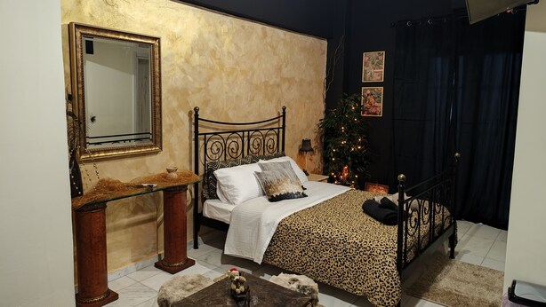 Une chambre à coucher avec un lit, une table de chevet, un miroir, une commode et une petite table sur laquelle est posé un ours en peluche.