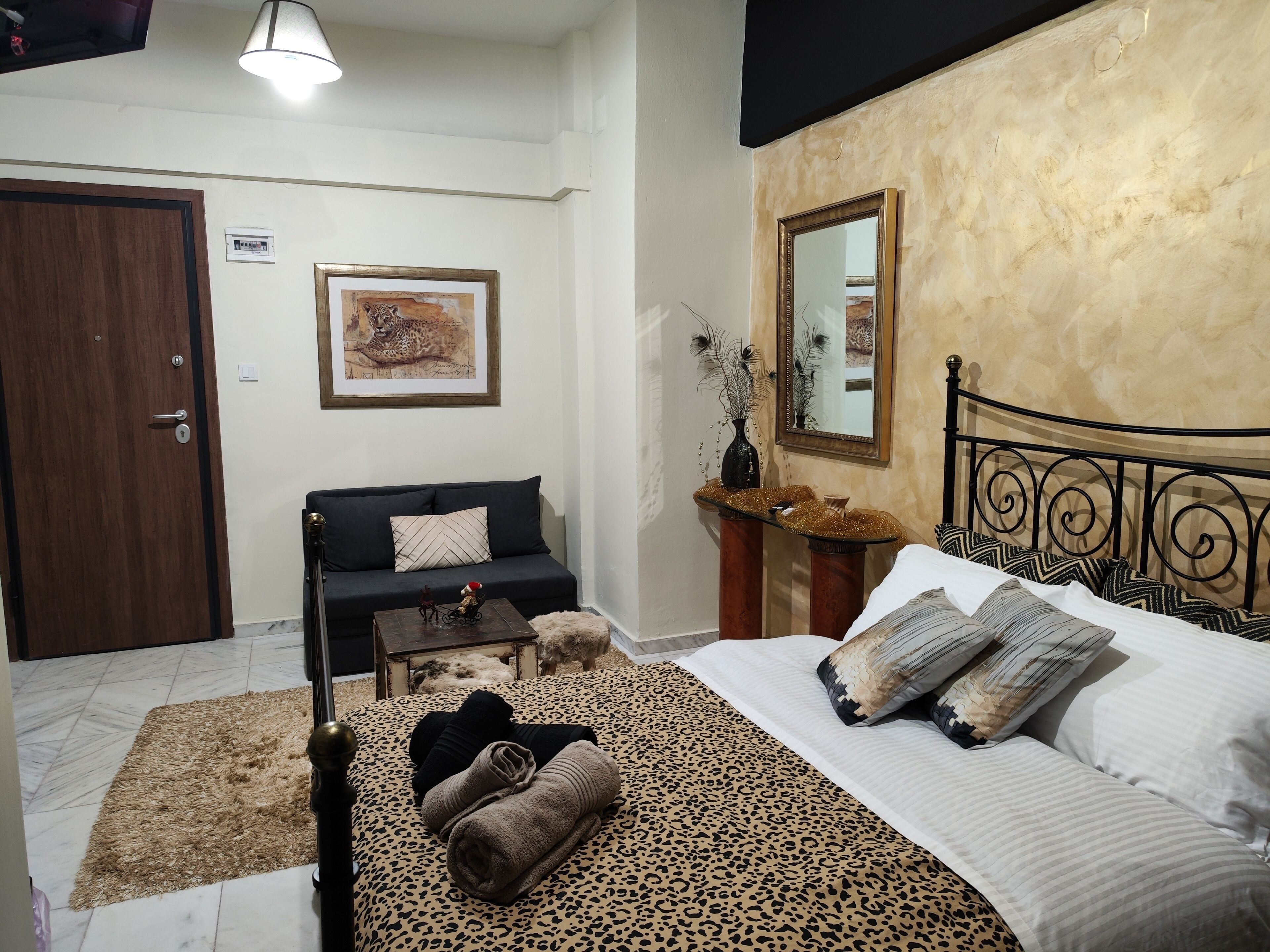 Quarto com cama, sofá, mesa pequena, espelho e porta.