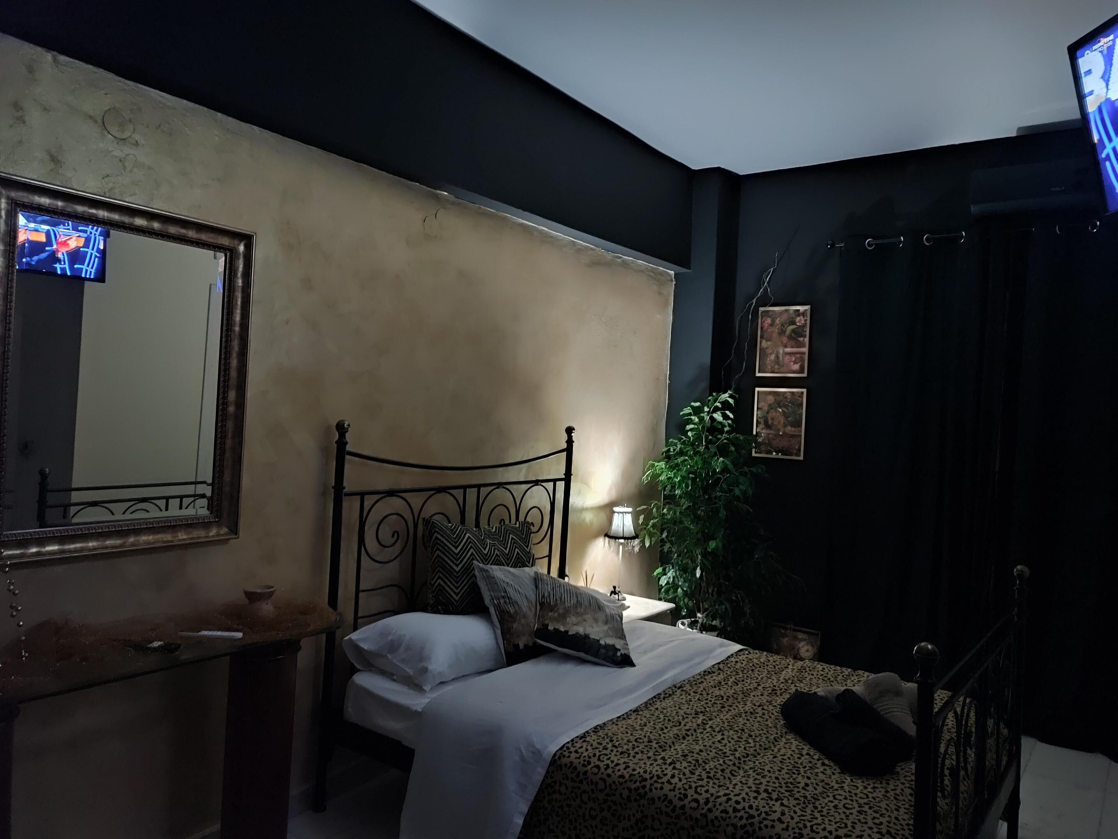 A bedroom with a bed, a bedside table, a mirror, a lamp, and a TV.
