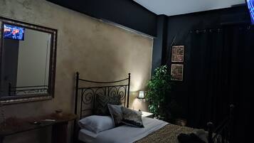 A bedroom with a bed, a bedside table, a mirror, a lamp, and a TV.