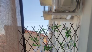 Un balcon avec une rambarde en treillis métallique, une petite table sur laquelle est posée une plante en pot et un tissu blanc.