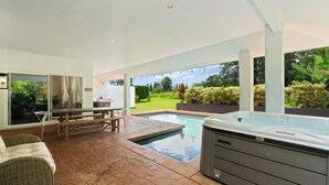Een terras met een hottub, een eettafel en een rieten bank.