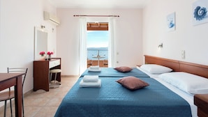 A hotel room with two beds, a desk, a chair, and a view of the sea through a window.