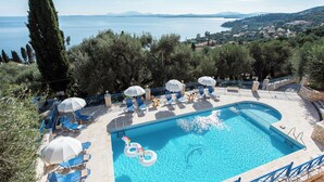 A swimming pool with lounge chairs and umbrellas, surrounded by trees and overlooking a body of water.