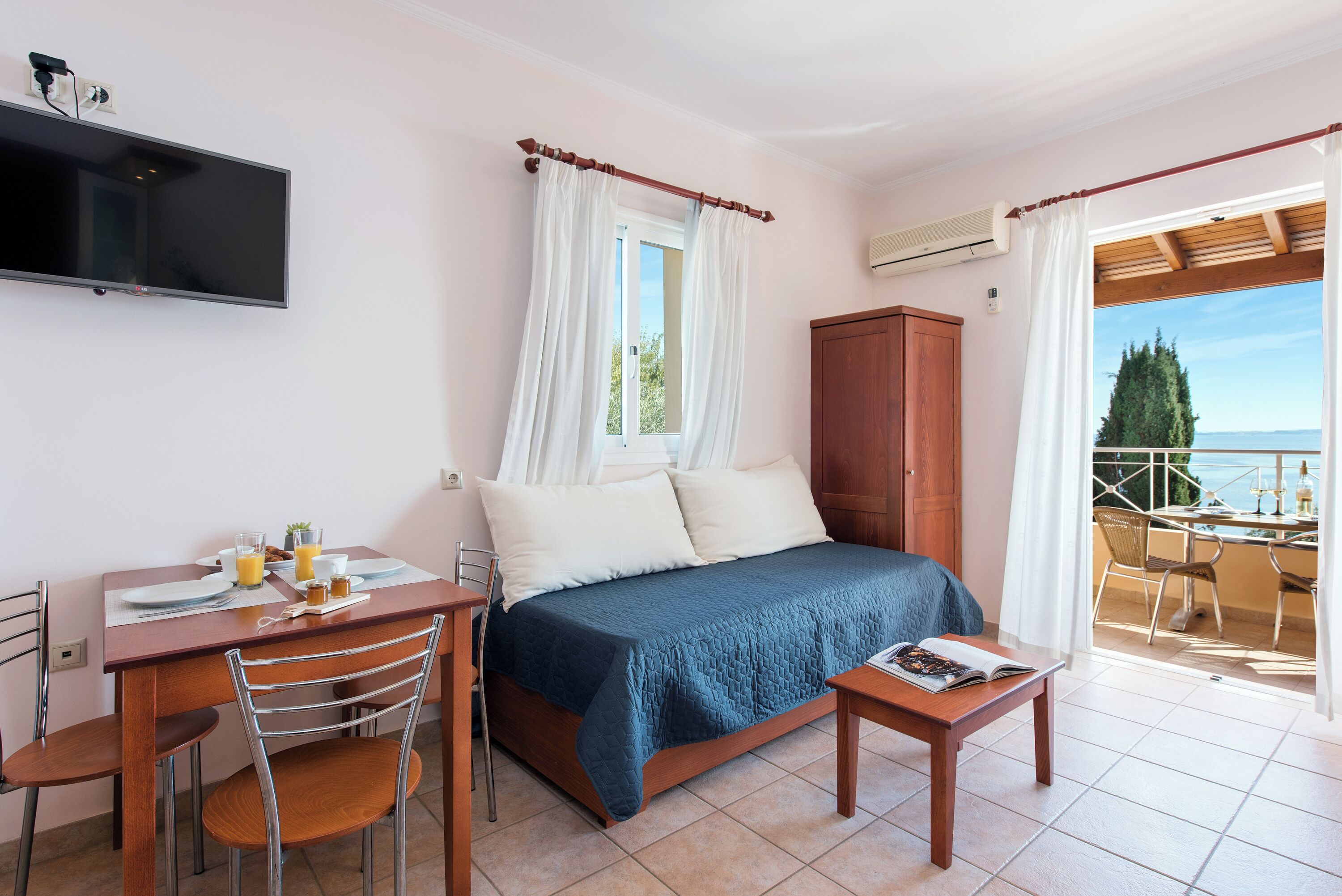 A bedroom with a bed, a desk with breakfast items, a TV, and a balcony with a view.