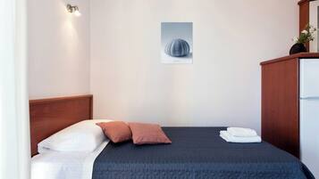 Una cama bien tendida con un edredón oscuro, dos almohadas y una manta blanca. Un cuadro enmarcado cuelga de la pared sobre la cama.