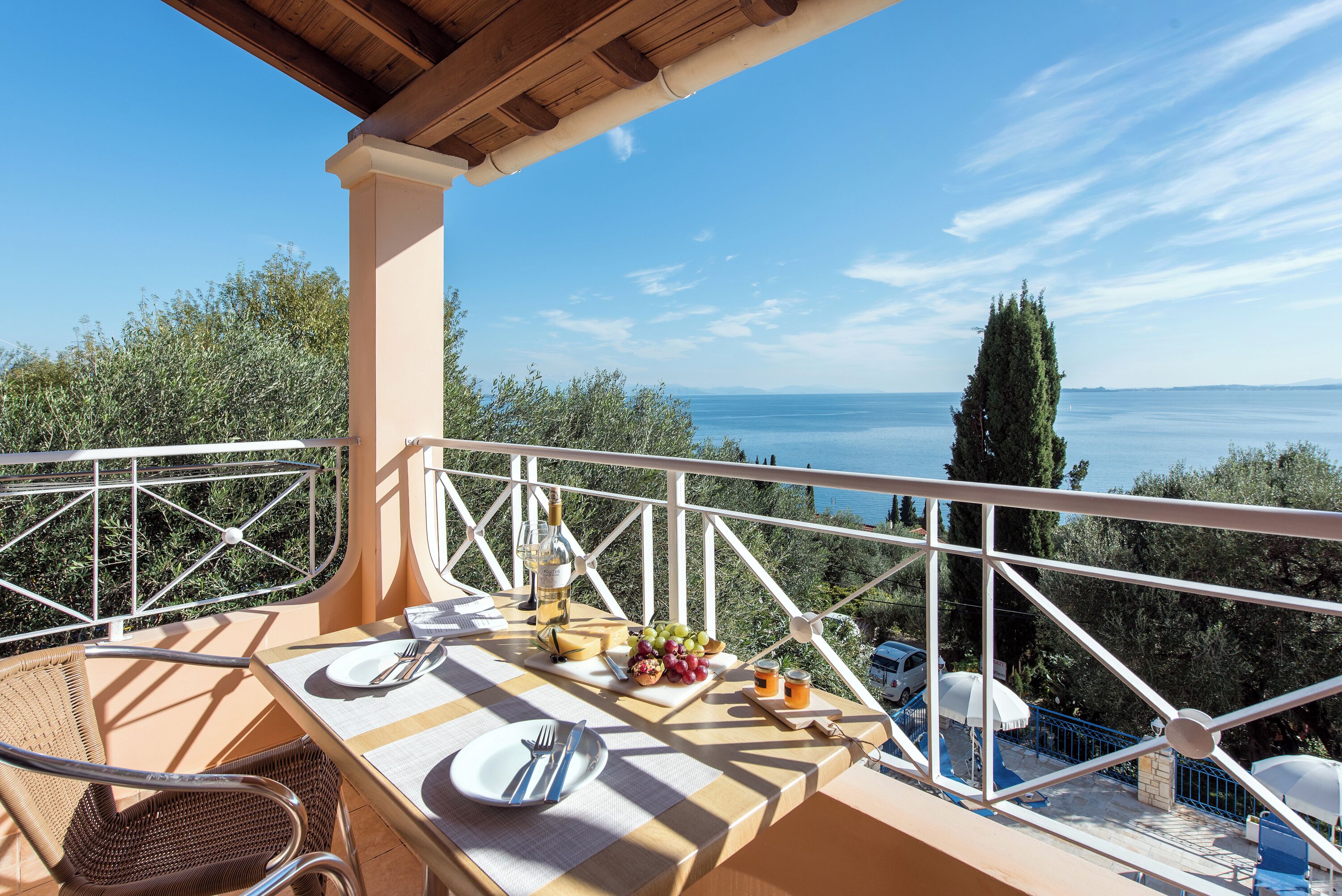 A balcony with a table set for two, overlooking a scenic view of the sea and trees.