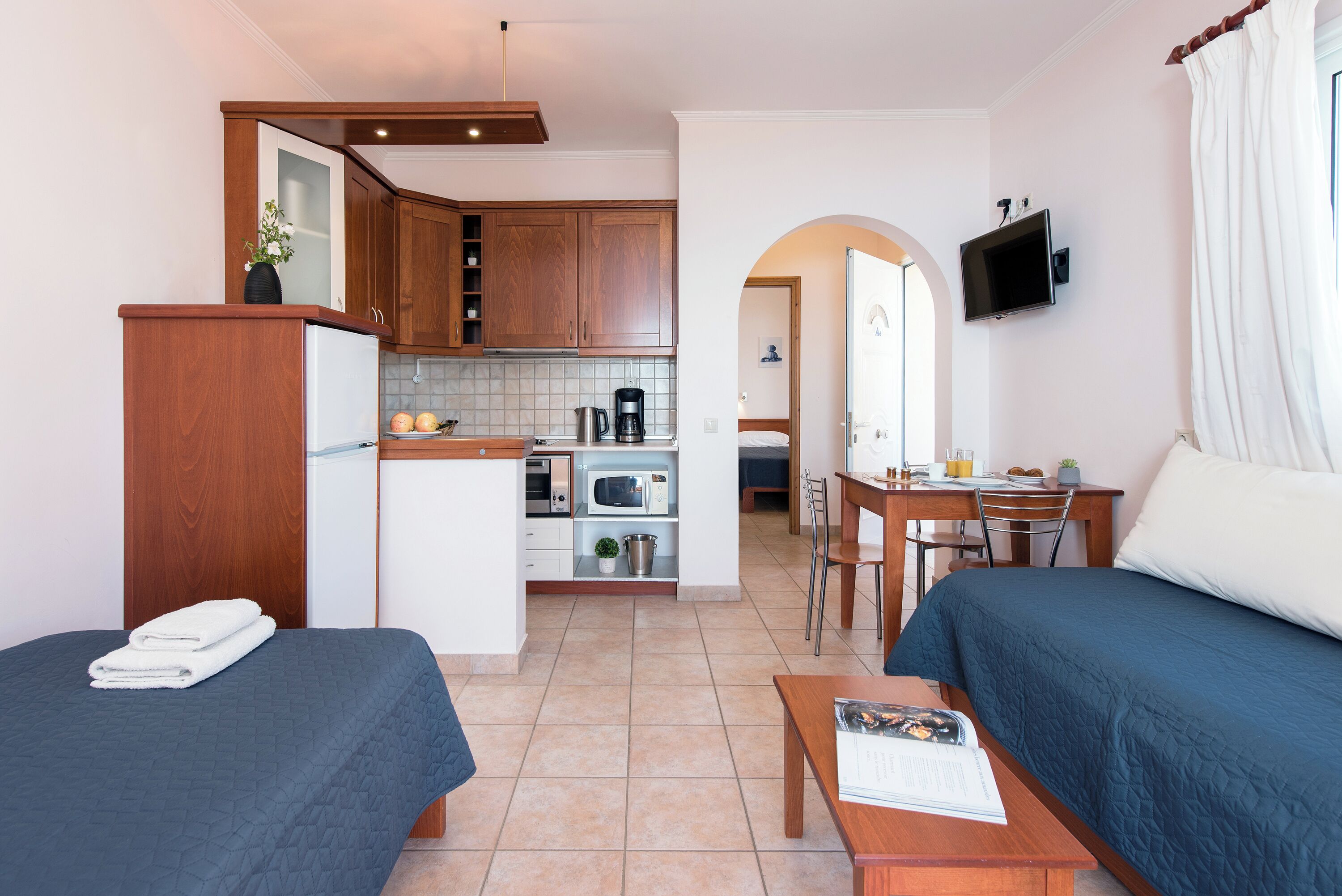Une chambre d’hôtel compacte comprenant un coin cuisine, deux lits, un espace repas et un téléviseur.