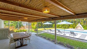An outdoor patio with a wooden table and chairs, a pool with lounge chairs, and a view of greenery. - 4br Biscayne River Home: Pool & Pickleball Fun 4 Bedroom Home (North Miami Beach)