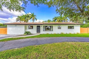 A single-story house with a white exterior, a black front door, and a small front yard with grass and a palm tree.