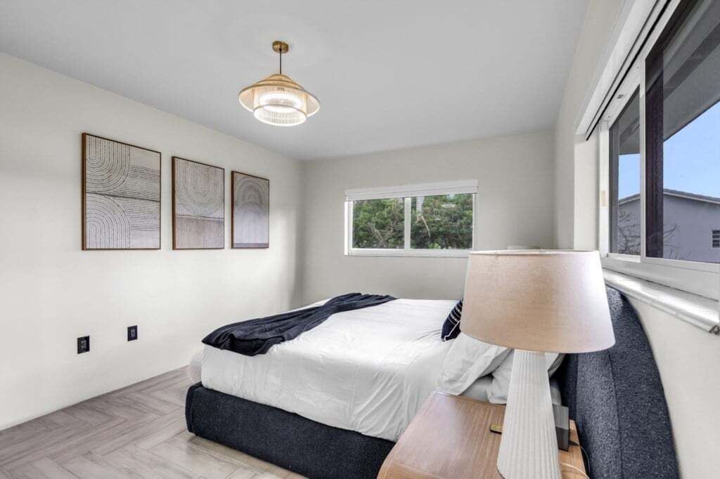 A modern bedroom with a bed, a bedside table, a lamp, and three wall-mounted artworks.