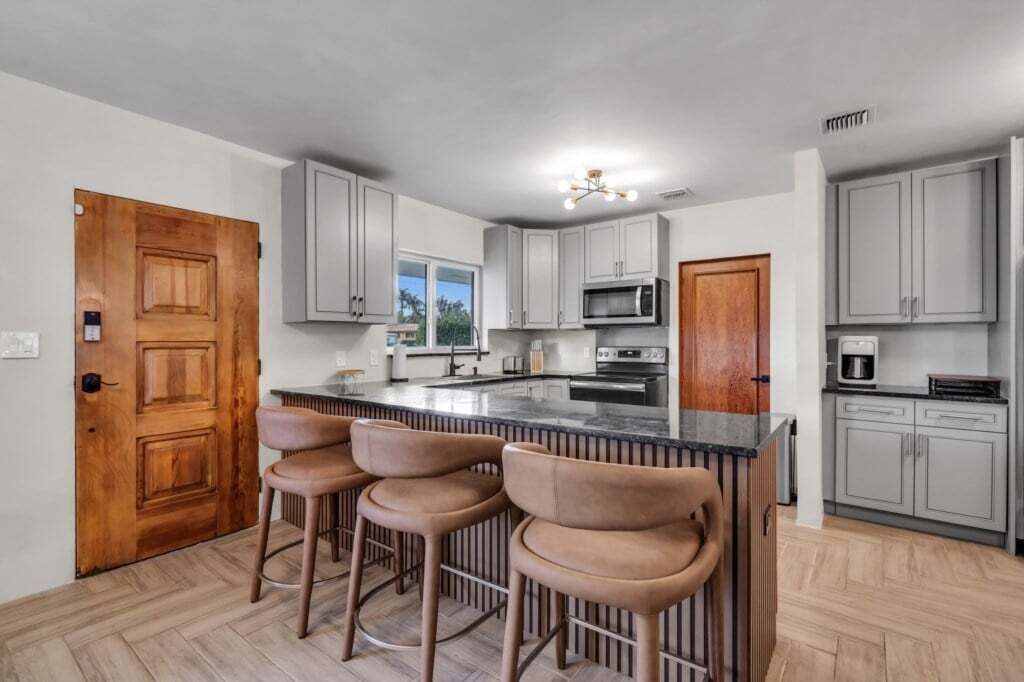 Eine moderne Küche mit grauen Schränken, einer zentralen Kochinsel mit Barhocker und einer Holztür.