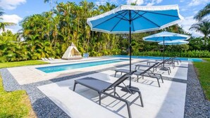 A pool area with lounge chairs and umbrellas, surrounded by palm trees. - 4br Biscayne River Home: Pool & Pickleball Fun 4 Bedroom Home (North Miami Beach)