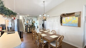 A dining area with a wooden table and chairs, a kitchen with a stainless steel refrigerator, and a map on the wall. - Windsail 6 Bedroom Home (Navarre)