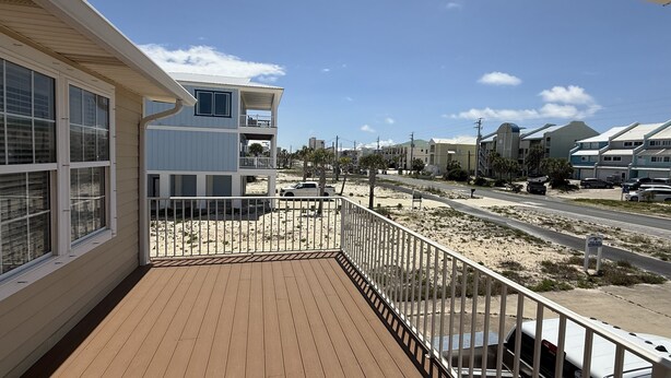 A balcony with a wooden deck, overlooking a street with parked cars and buildings. - Windsail 6 Bedroom Home (Navarre)