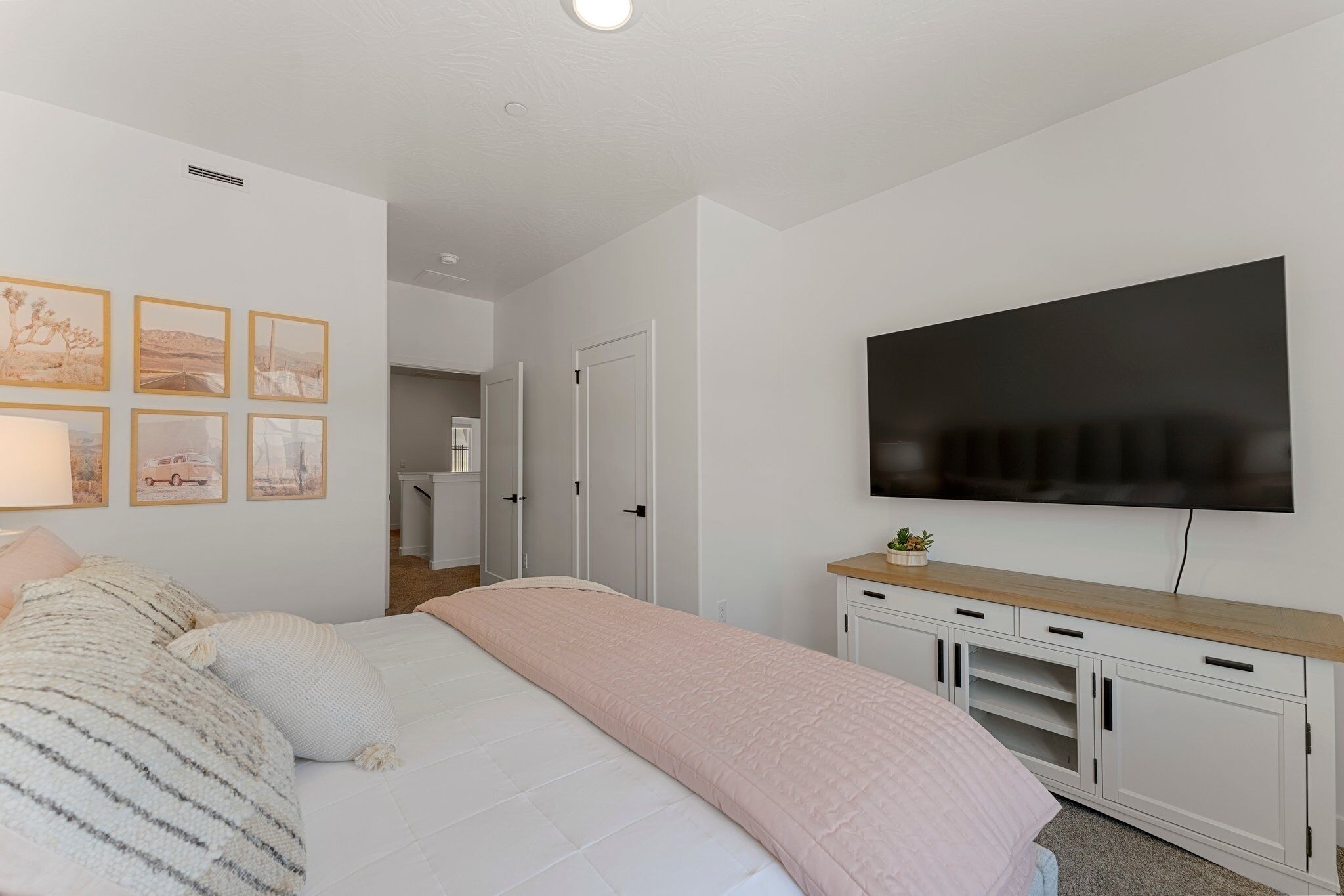 Een slaapkamer met een bed, een aan de muur bevestigde televisie en een tv-meubel met een plant.