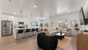 A modern kitchen with white cabinets, a stainless steel refrigerator, a microwave, and a bar area with black chairs. - Sand Hollow Skyline 4 Bedroom Townhouse (Washington)