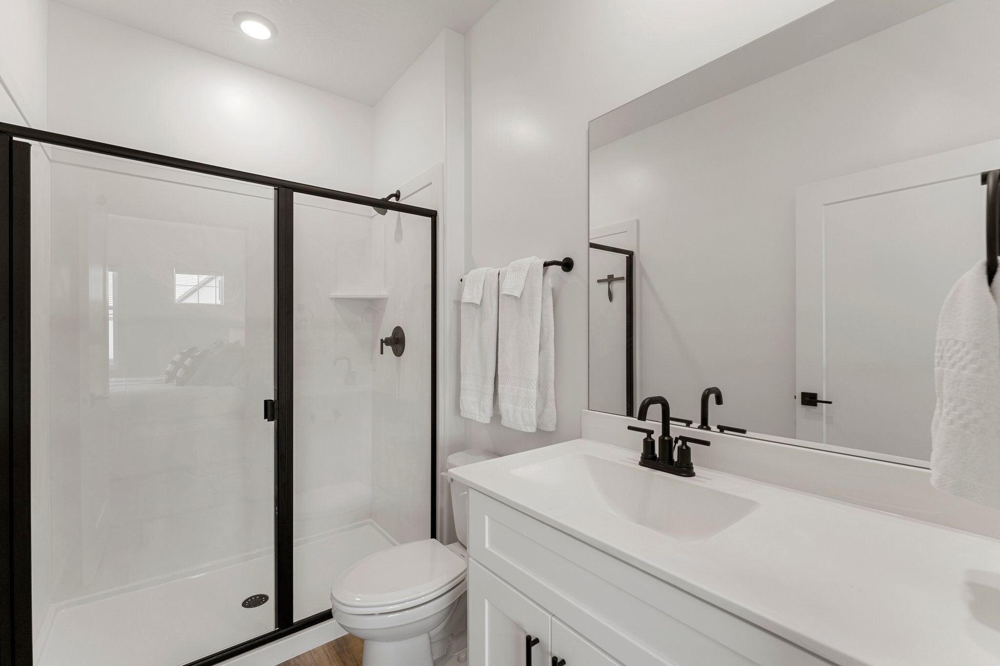 Un bagno moderno con box doccia in vetro, un water bianco, un lavandino bianco con rubinetto nero e uno specchio grande sopra il lavandino.