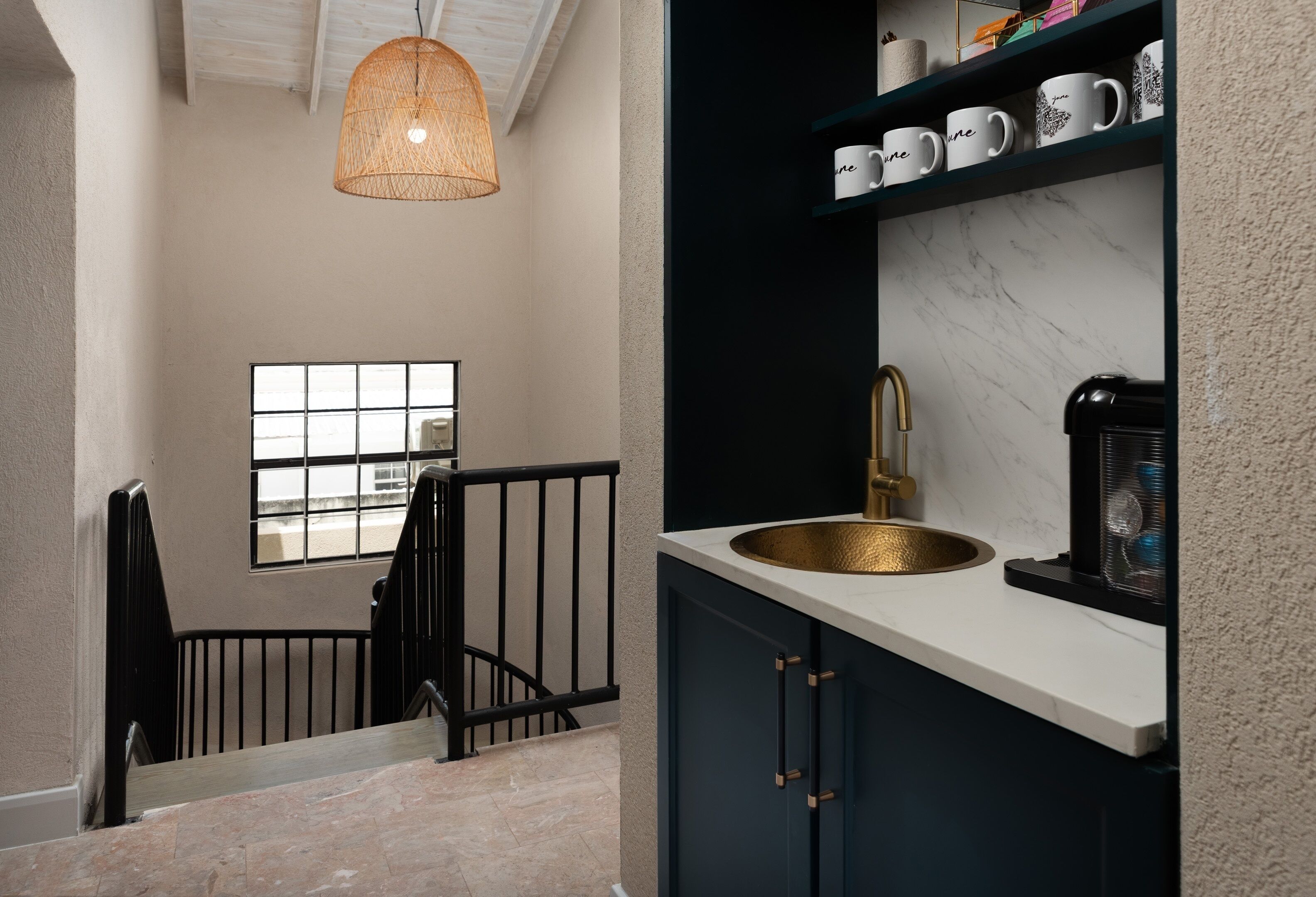 Una cocina con encimera blanca, pileta dorada y cafetera. Se ve una ventana con vistas al exterior.