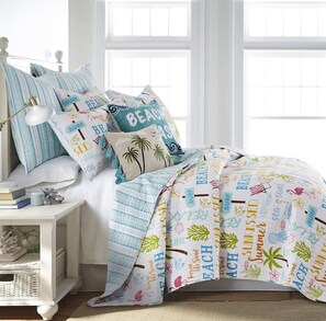 Een slaapkamer met een bed voorzien van een beddegoed met een strandthema, een nachtkastje met boeken en een lamp, en een raam met uitzicht op de lucht.