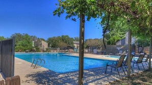 Una piscina con sillas de descanso, rodeada de árboles y un cielo despejado.