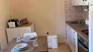 A compact kitchen with a sink, stove, and cabinets. There is a table with plates and a glass.