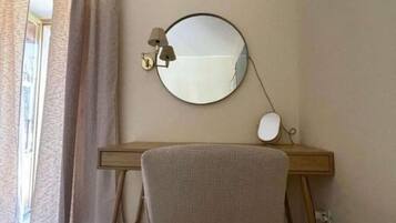 Una habitación con un espejo redondo en la pared, un escritorio con una lámpara y una silla.