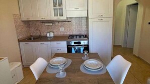 A compact kitchen with white cabinets, a gas stove, and a dining table set for two.