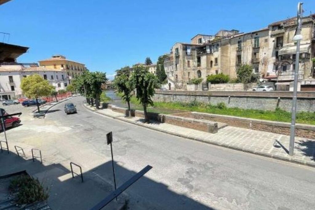 Straßenansicht mit Gebäuden, blauem Himmel und geparkten Autos.