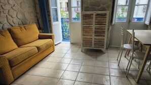 A room with a yellow patterned sofa, a wooden cabinet, a dining table with chairs, and a stone wall.