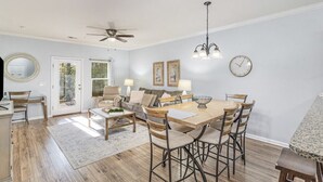 Un salon spacieux avec une table à manger en bois, des sièges confortables et un ventilateur de plafond.
