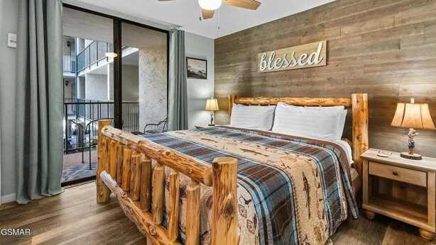 A bedroom with a wooden bed frame, a ceiling fan, a 'blessed' sign on the wall, and a view of the outside balcony. - Slopeside Serenity 111–Cabin Vibe–Sleeps 4 (Gatlinburg)