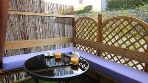 Un banco de madera con respaldo de celosía y asiento acolchado, junto a una mesa redonda de vidrio con estructura negra.