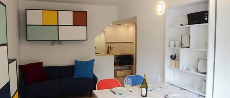 Una sala de estar moderna con una mesa blanca dispuesta para comer, un sofá azul oscuro con cojines de colores y una obra de arte abstracta colgada en la pared.