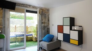 Una habitación con puerta de cristal corredera que da a un espacio exterior, un sofá gris con un cojín azul y una obra de arte geométrica colgada en la pared.