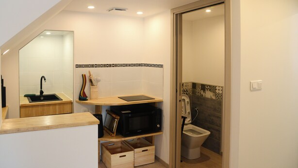 Un baño moderno con tocador de madera, microondas negro y un inodoro con un revestimiento de azulejos decorativos.
