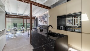 A modern kitchen with a black marble island, a built-in oven, and a large window overlooking a balcony with outdoor seating. - Waou Gran Via VII - Alquiler Corta Duración (Madrid)