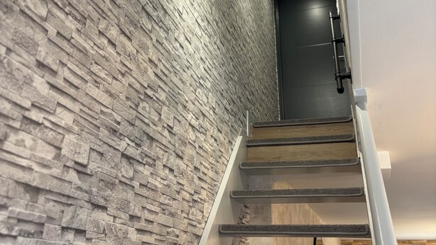 Un escalier moderne avec un mur en pierre à texture, des marches en bois et une rampe en métal.
