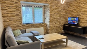 Un salon moderne avec un mur en pierre, un canapé, une table basse et un téléviseur posé sur un meuble noir.