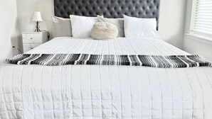Una cama bien hecha con un cabecero gris tapizado, ropa de cama blanca y una almohada decorativa.