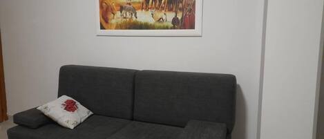 A dark grey sofa with a floral pillow against a white wall, with a painting of a savannah scene above it.