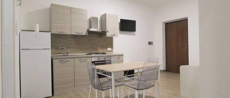 A modern kitchen with light wood cabinets, a built-in stove, and a dining area with a glass table and chairs.