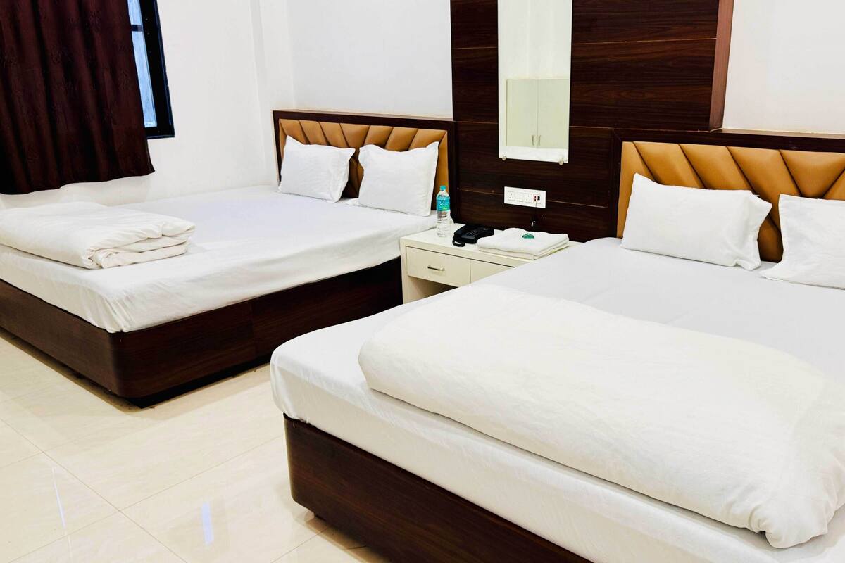 A hotel room with two single beds, a nightstand, a mirror, and a window with curtains.