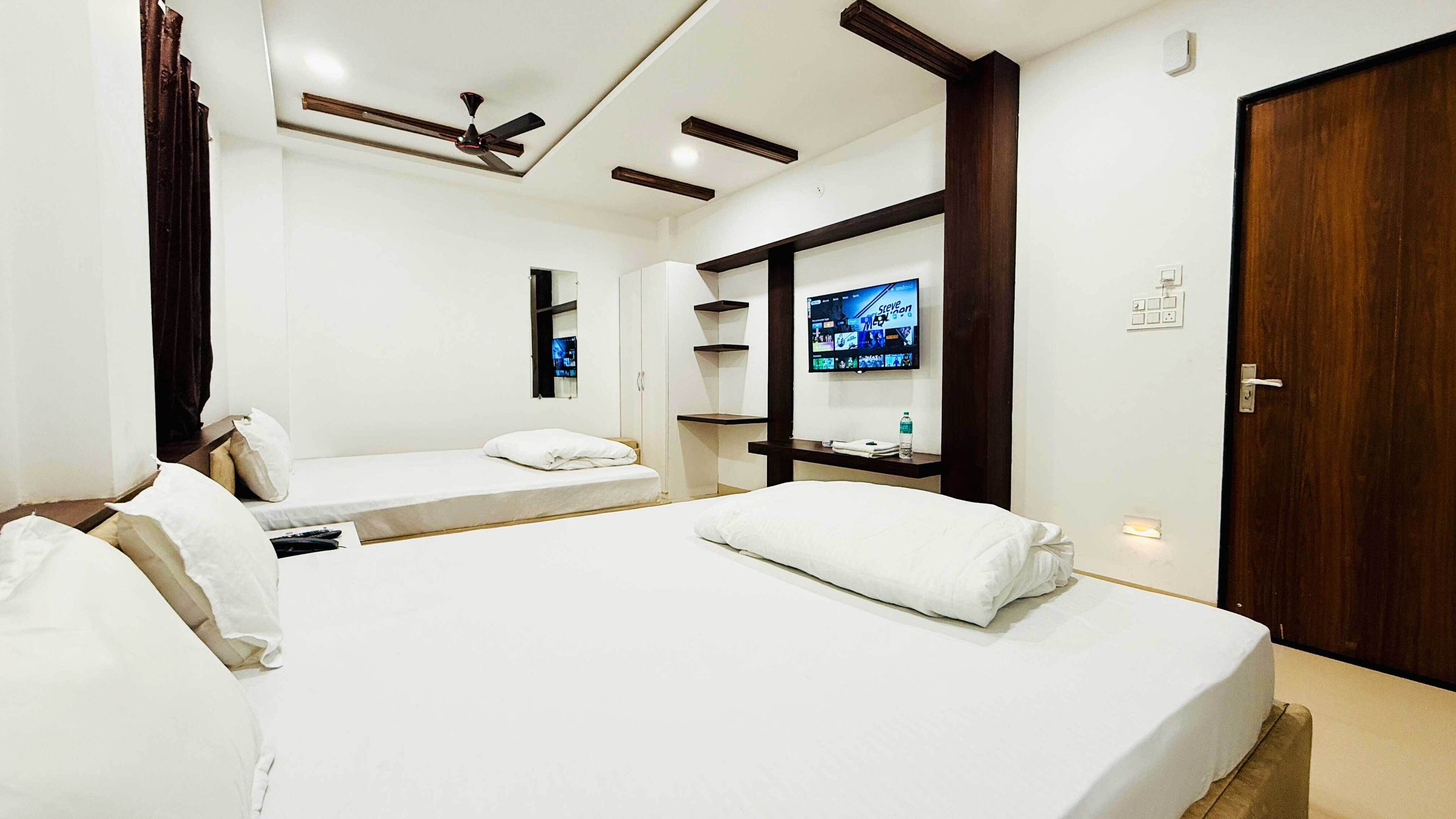 A hotel room with two beds, a TV mounted on the wall, a ceiling fan, and a wooden door.