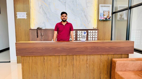 A reception desk with a marble wall and a check-out time sign. - Hotel Shree Rameshwaram (Khandwa)